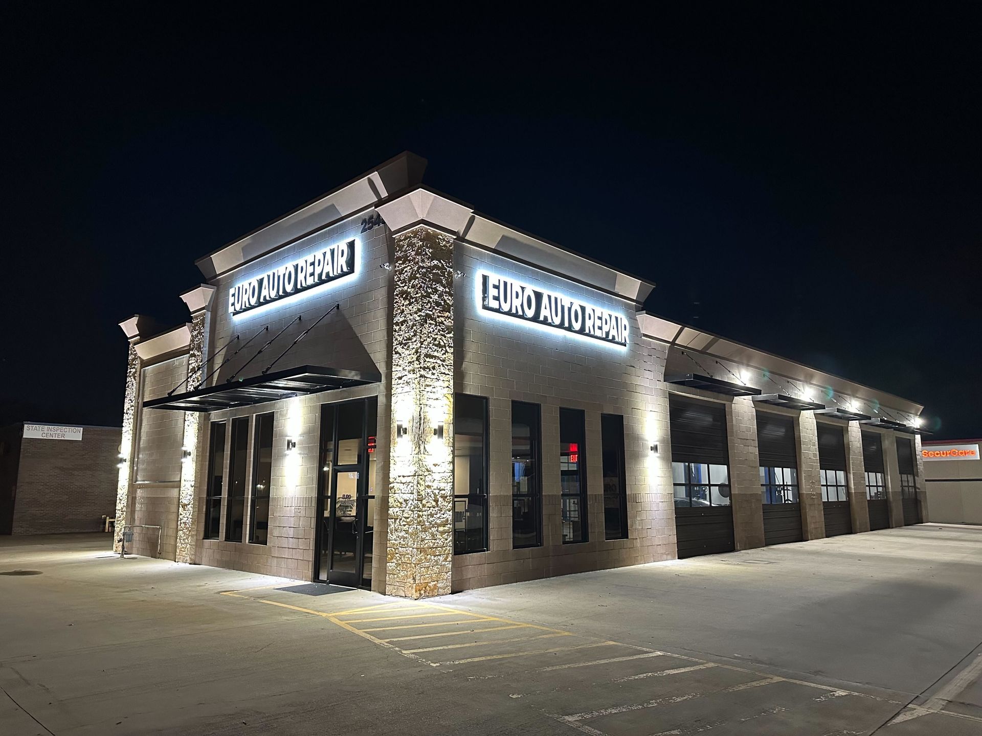 Illuminated auto repair shop at night, with signage, glass garage doors, and brick facade | Euro Auto Repair