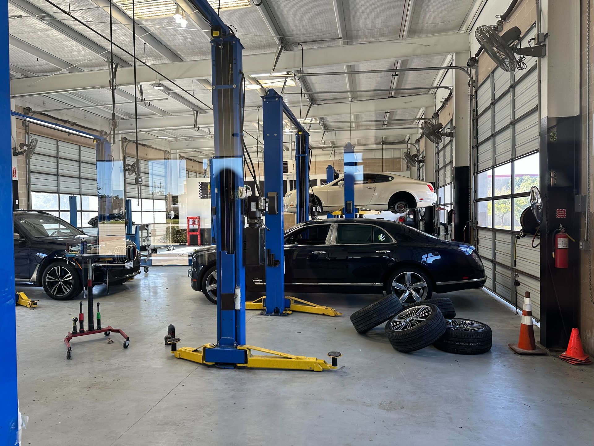 Inside a car repair shop, cars on lifts, mechanics' tools, tires, and open garage doors | Euro Auto Repair