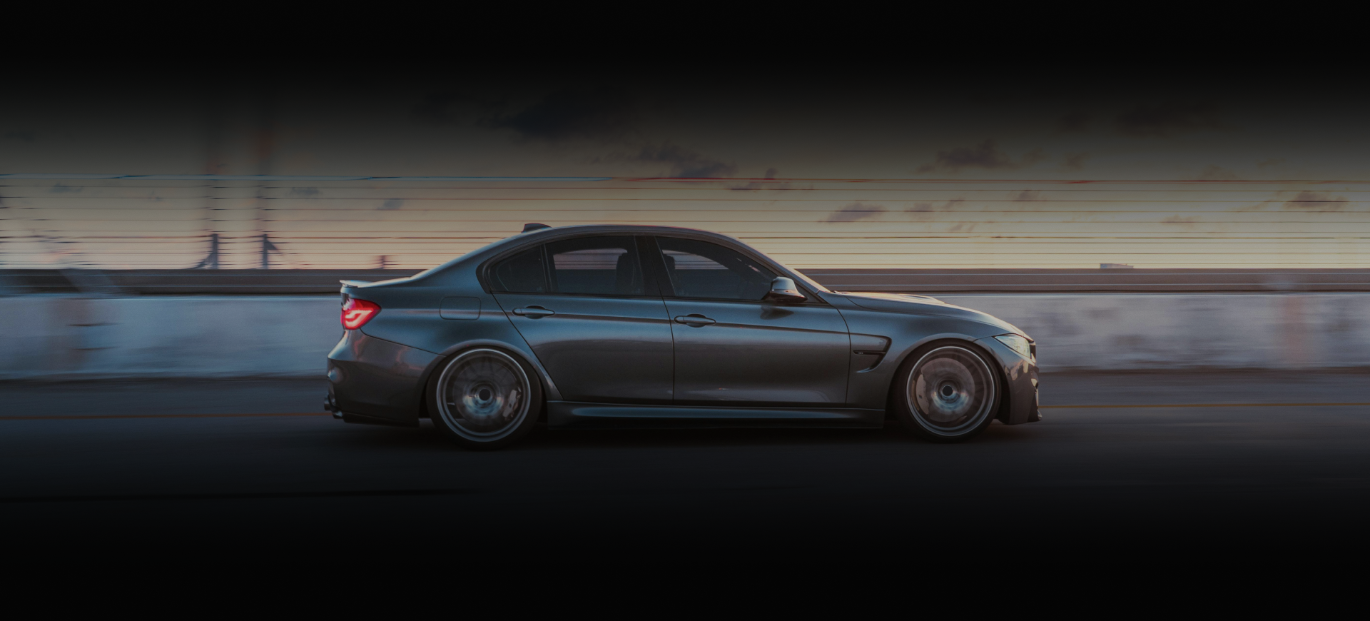 Gray BMW sedan driving on a road, side view. Low angle, dark background | Euro Auto Repair