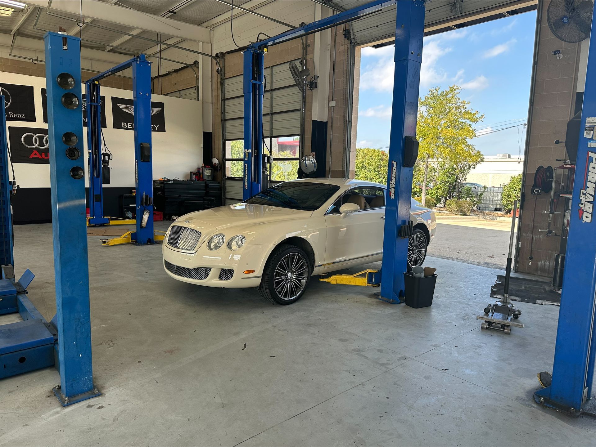 White Bentley inside auto repair shop, lifted by blue hydraulic lifts | Euro Auto Repair