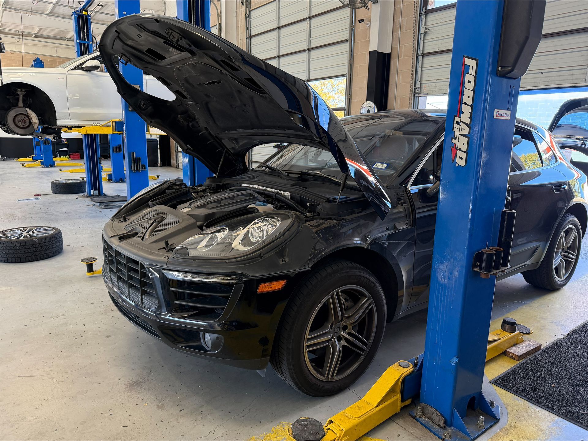 Black car in a repair shop with hood open, parked near a blue lift | Euro Auto Repair