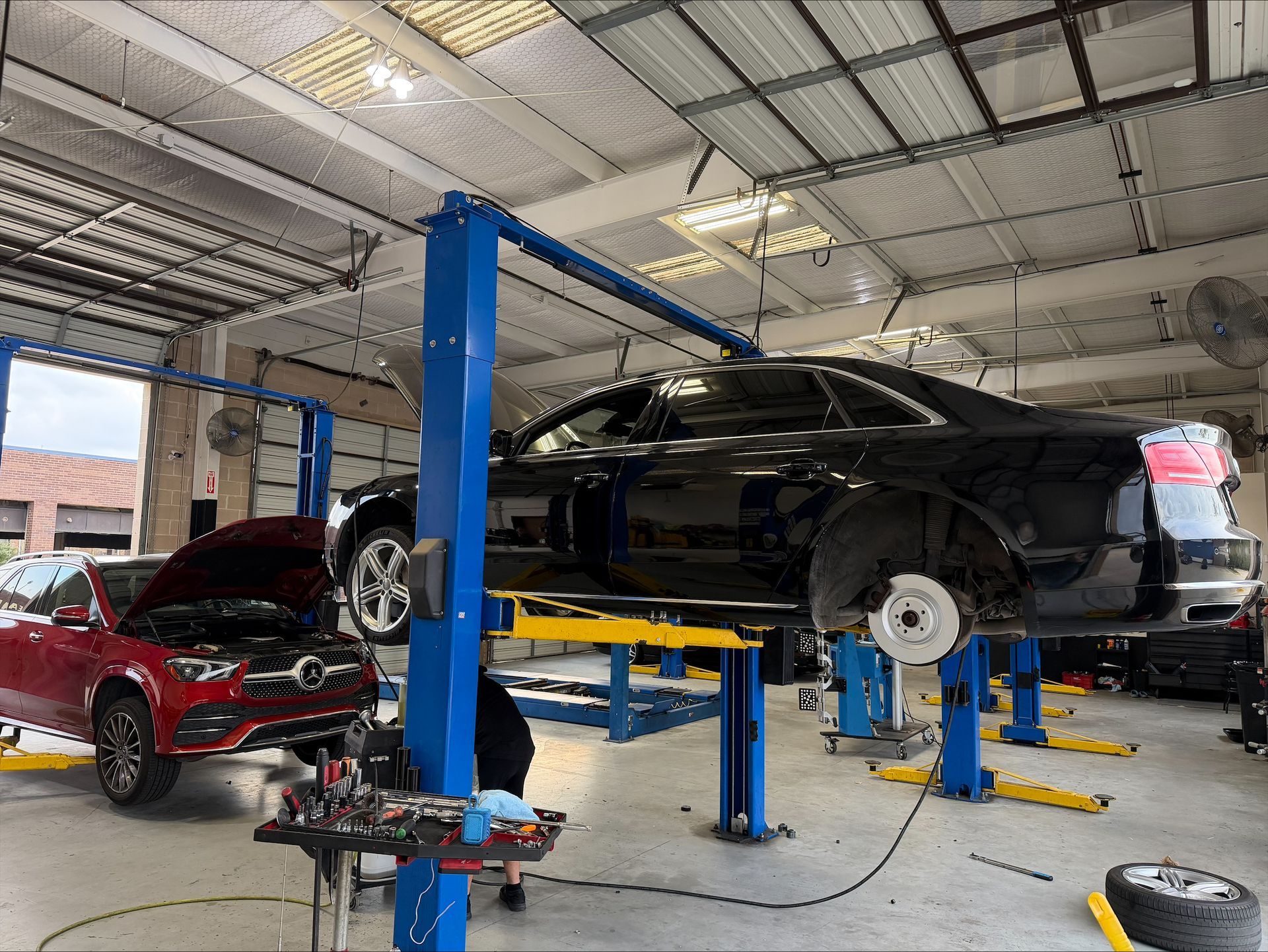 Cars in a repair shop: one on a lift, another with its hood open, tools visible | Euro Auto Repair