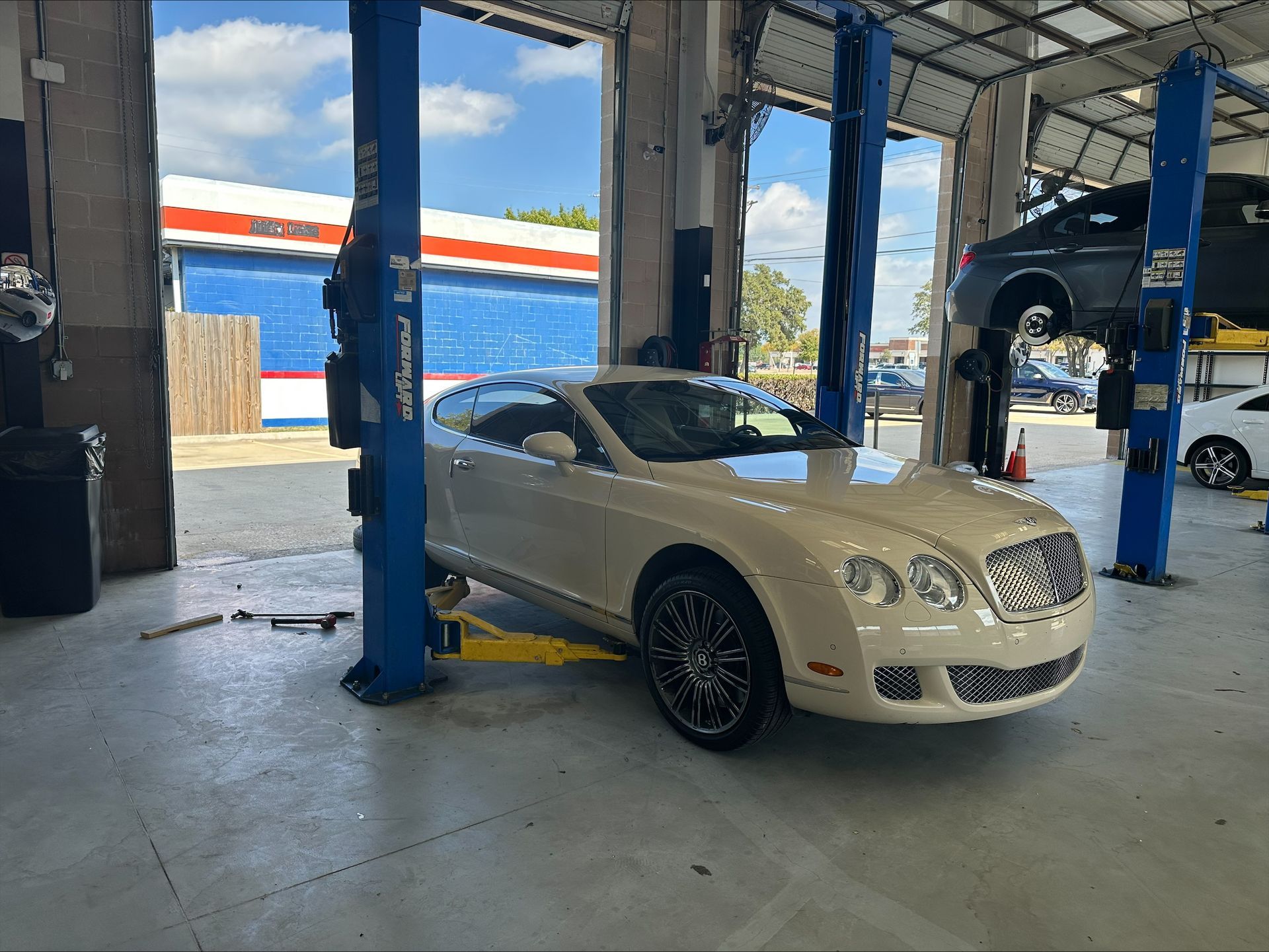 White Bentley on a car lift in a repair shop, other cars visible, sunny day | Euro Auto Repair