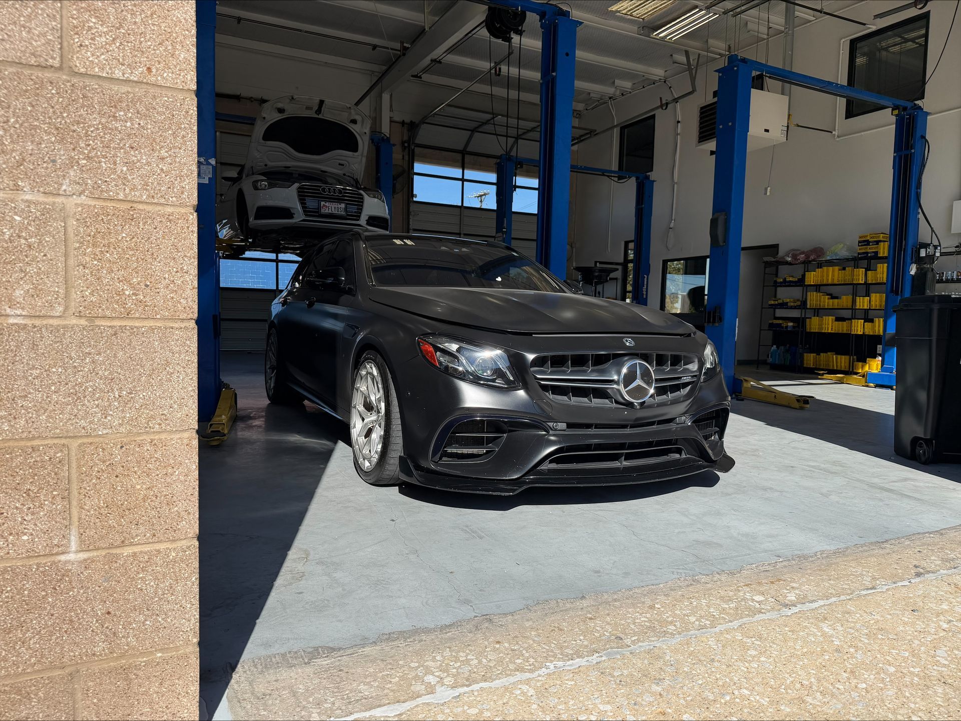 Dark gray Mercedes-Benz sedan inside a mechanic's shop. A second car is lifted overhead | Euro Auto Repair