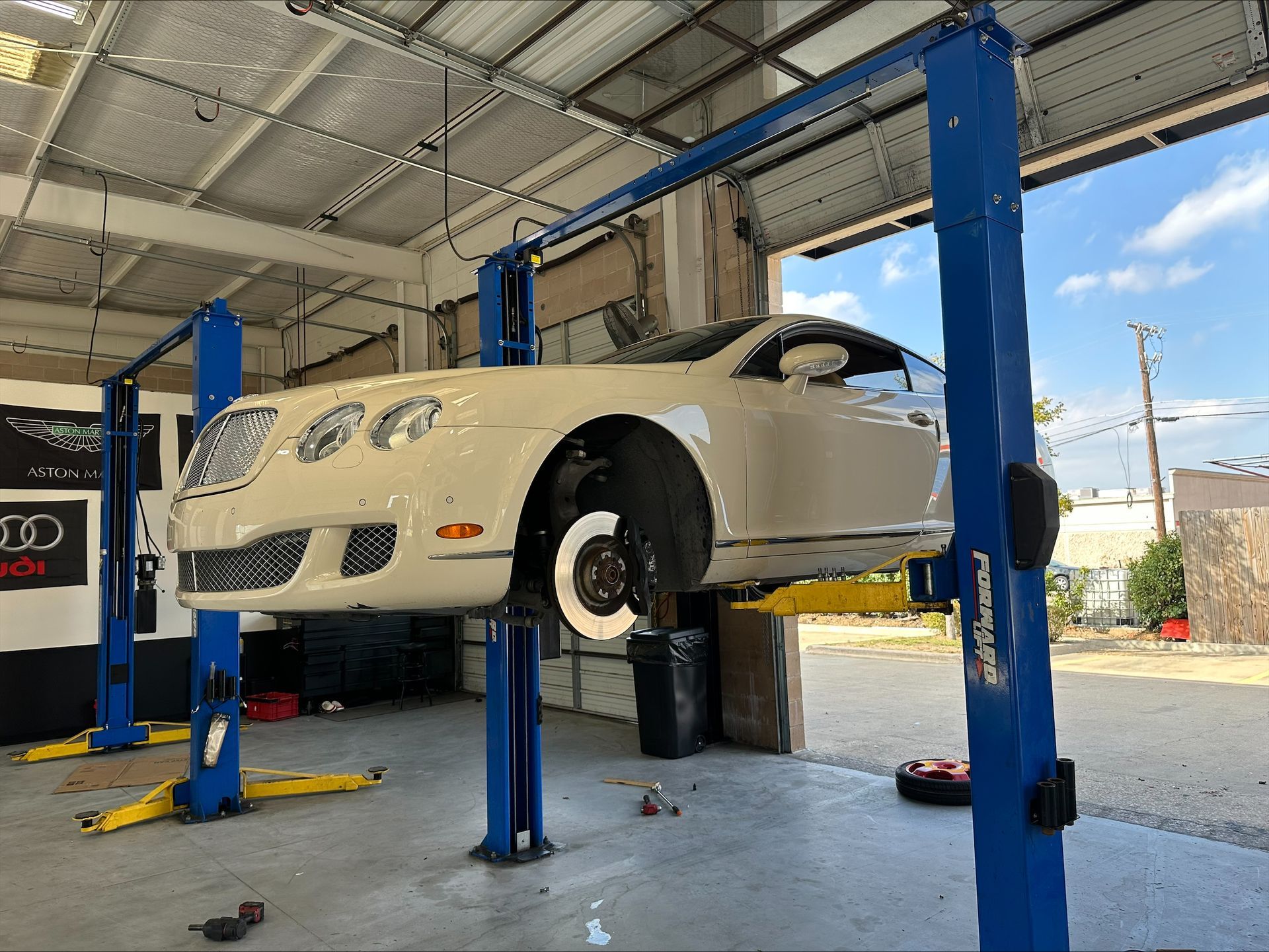 A white Bentley lifted on a car lift in a repair shop. One wheel removed, brake rotor visible | Euro Auto Repair