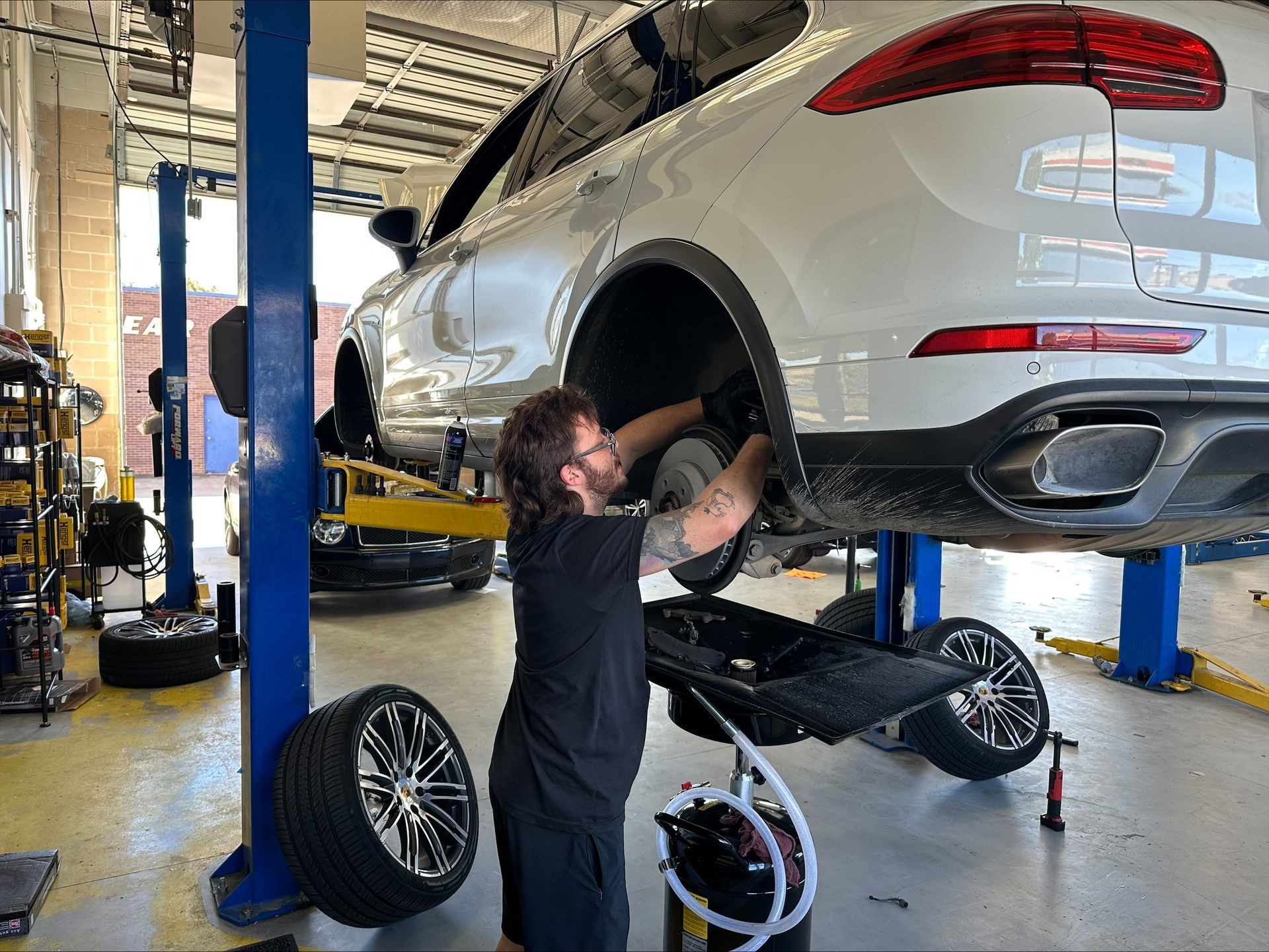 Mechanic working on a white Porsche SUV, raised on a lift in a garage | Euro Auto Repair