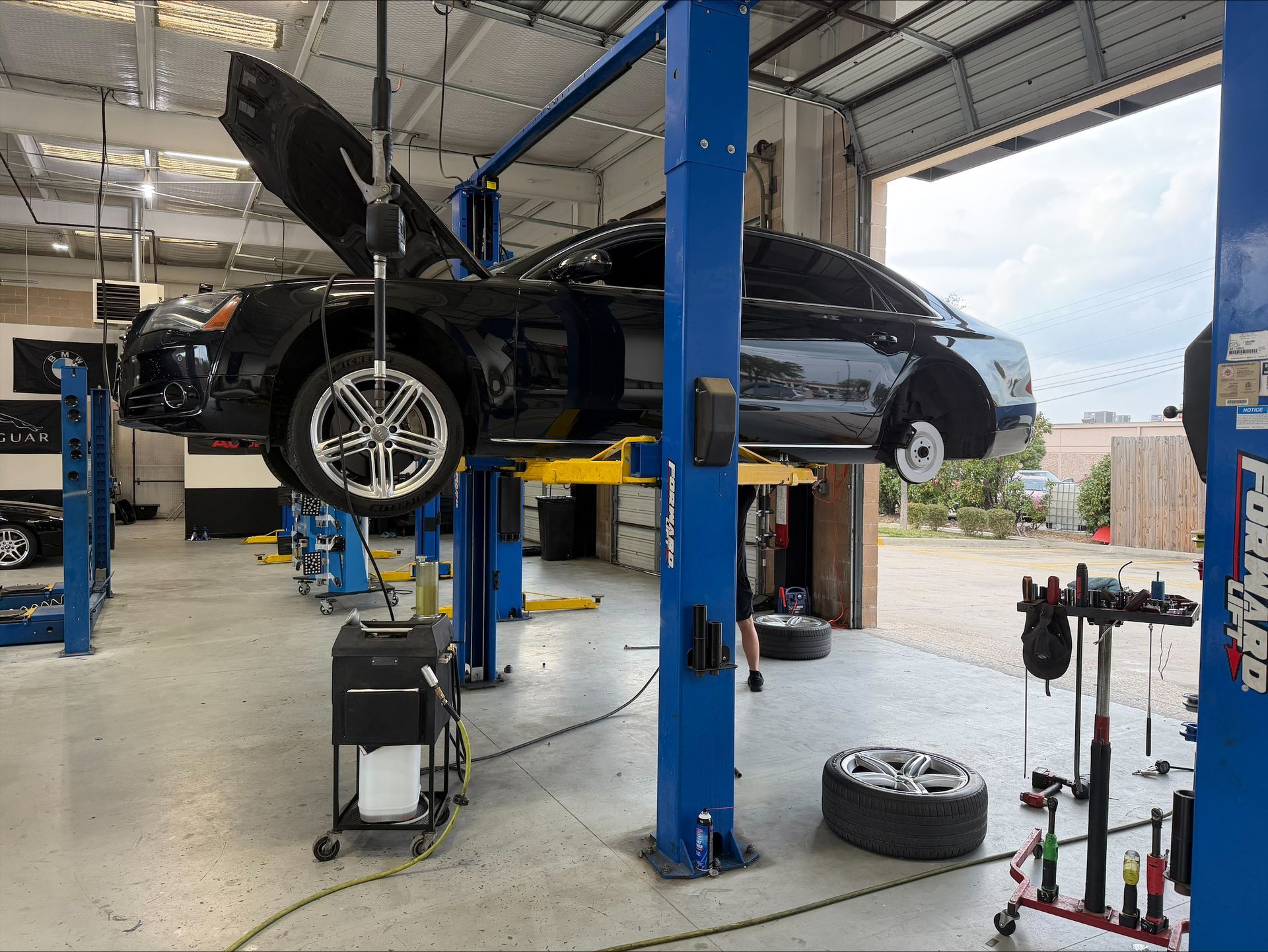 A black car is lifted in a garage, hood open. Tires and tools surround the vehicle | Euro Auto Repair