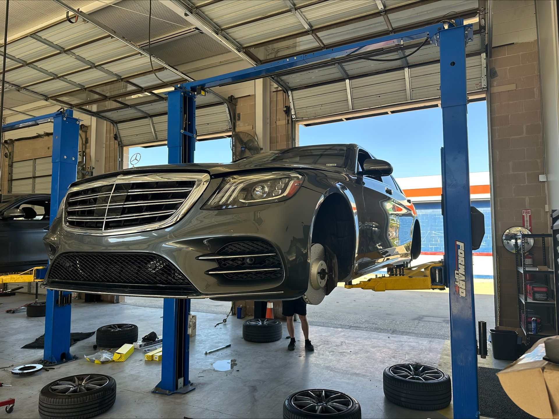 A gray Mercedes sedan raised on a car lift in a garage with tires on the floor | Euro Auto Repair