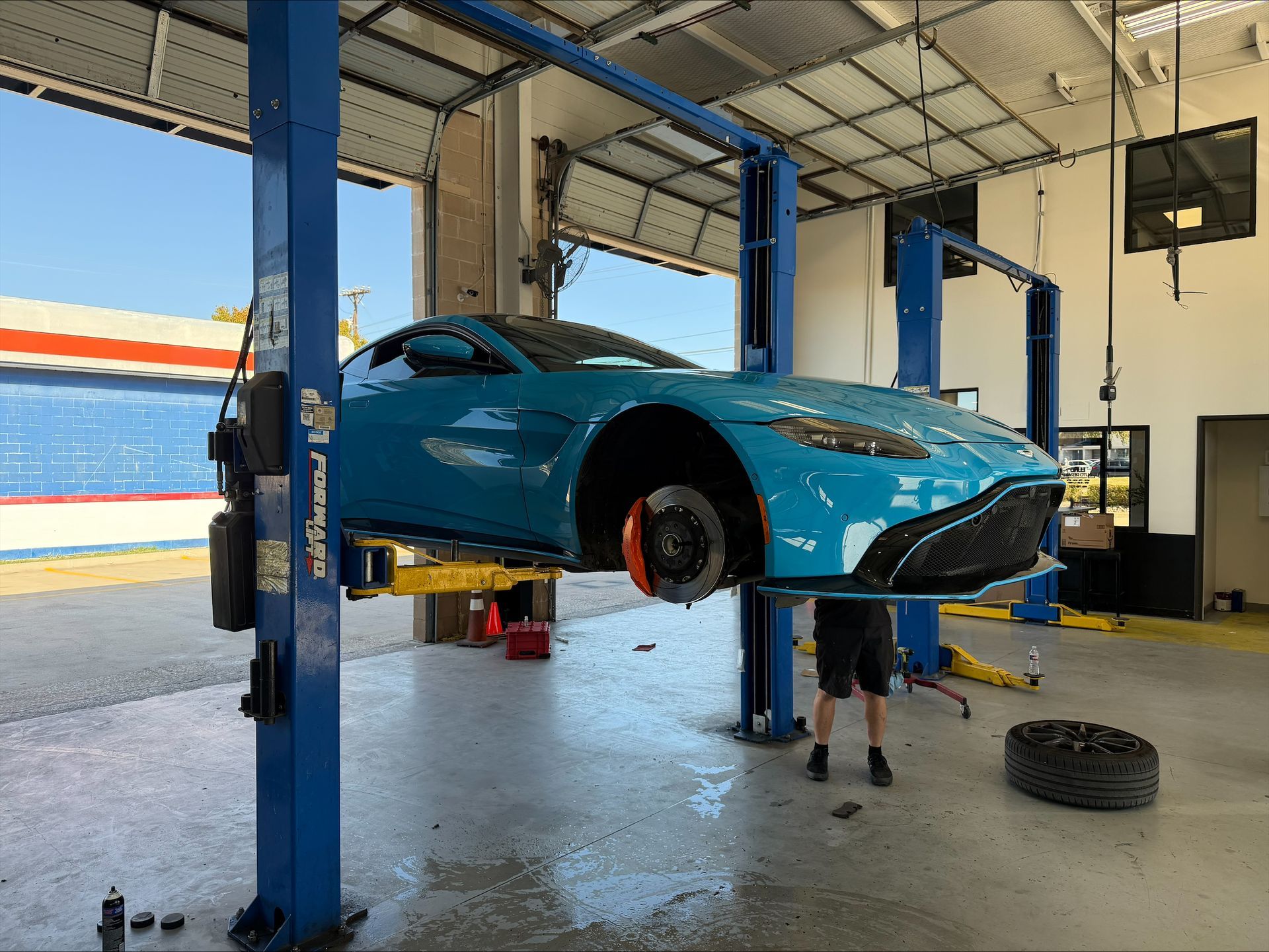 Blue Aston Martin car raised on a lift in a garage, undergoing repair. A person is working on the car | Euro Auto Repair