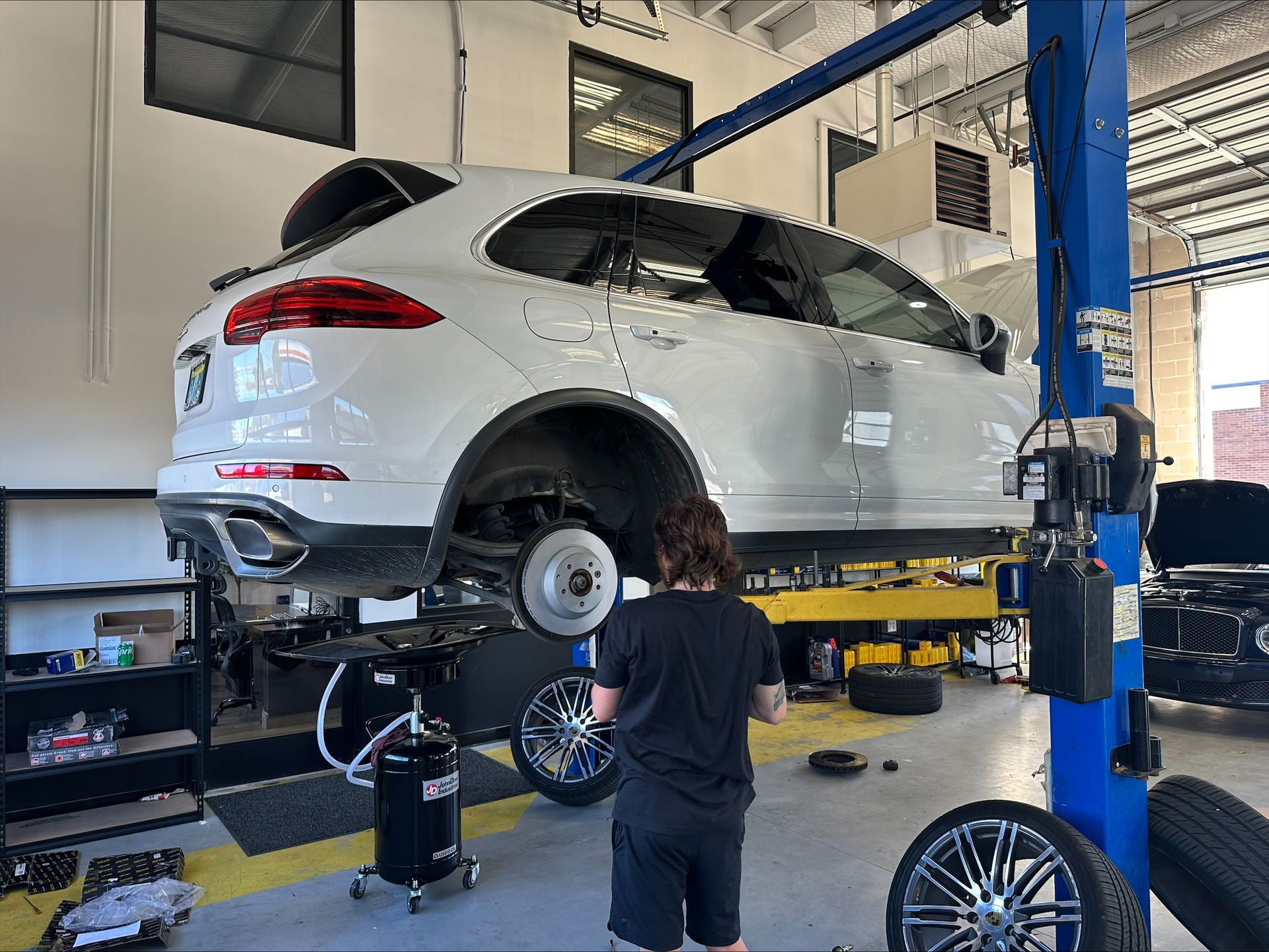 A white SUV on a lift in a garage, a person works on a rear wheel | Euro Auto Repair