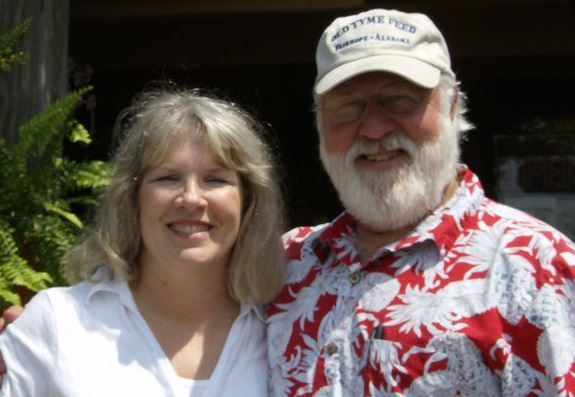 A man and woman posing for a picture with the man wearing a martinez hat