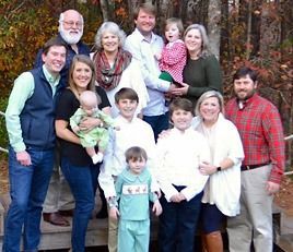 A large family is posing for a picture together in the woods.