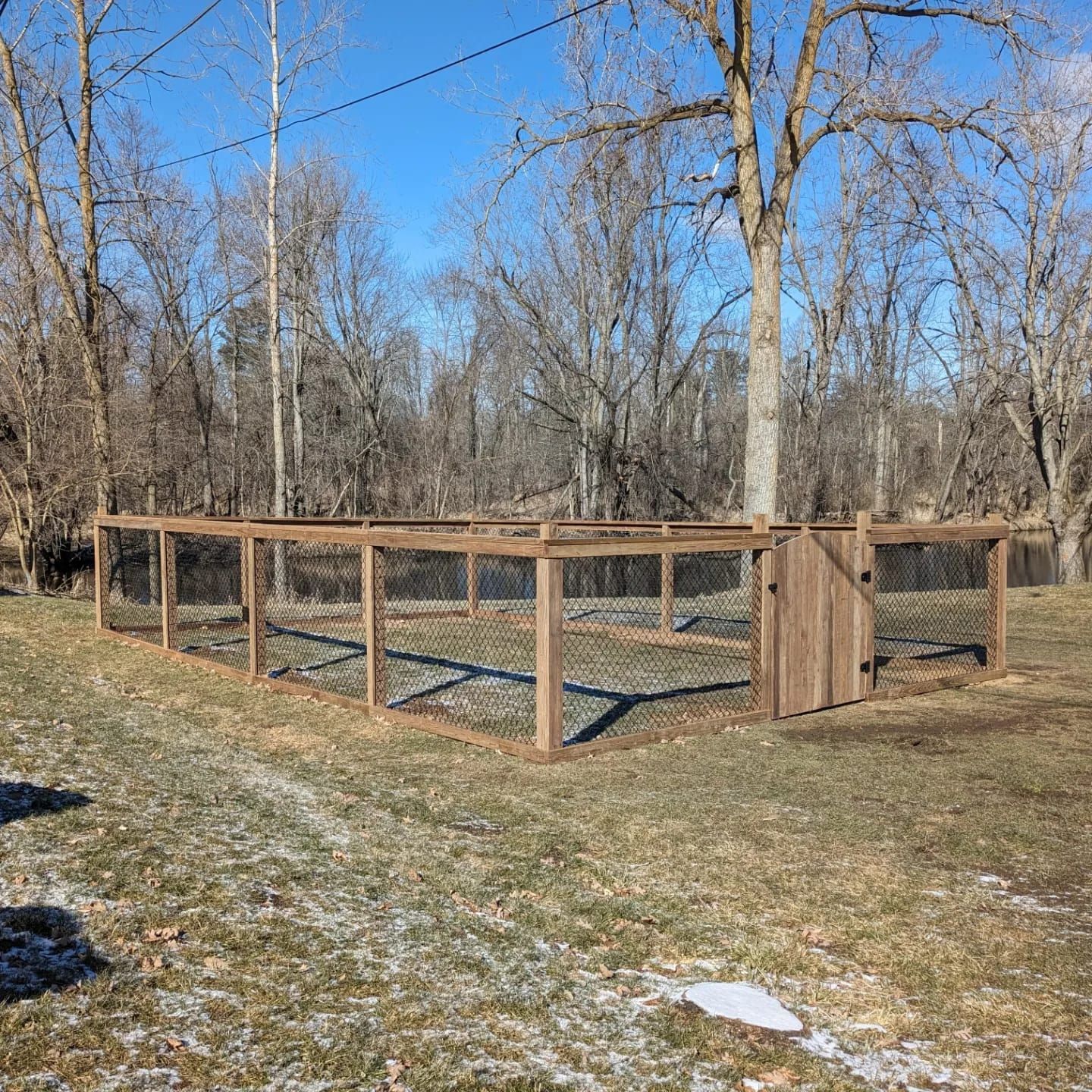 A rectangular garden enclosure with wooden posts and wire fencing, including a gate, set in a grassy yard near trees.