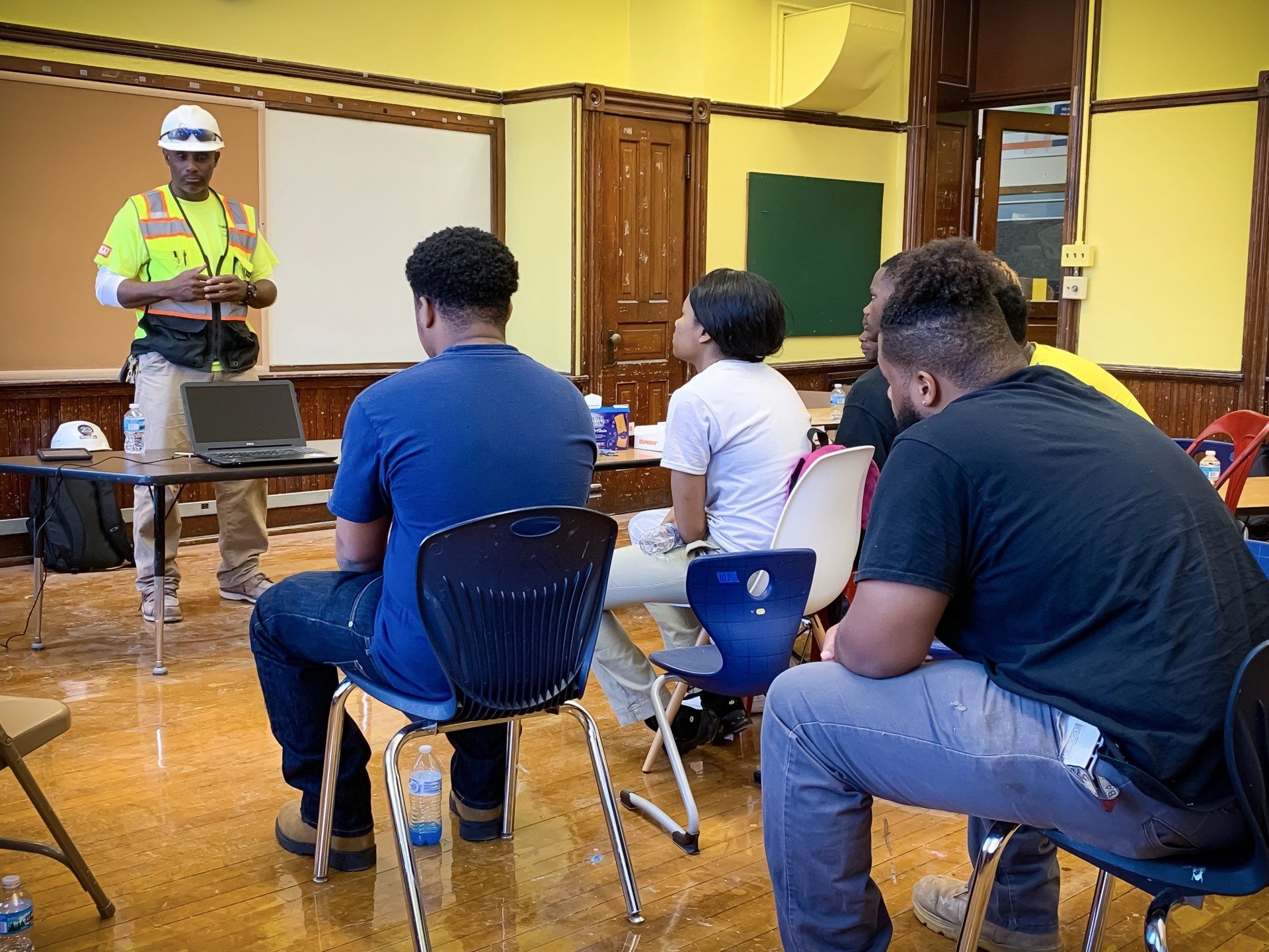 A man in a hard hat is giving a presentation to a group of people sitting in chairs.