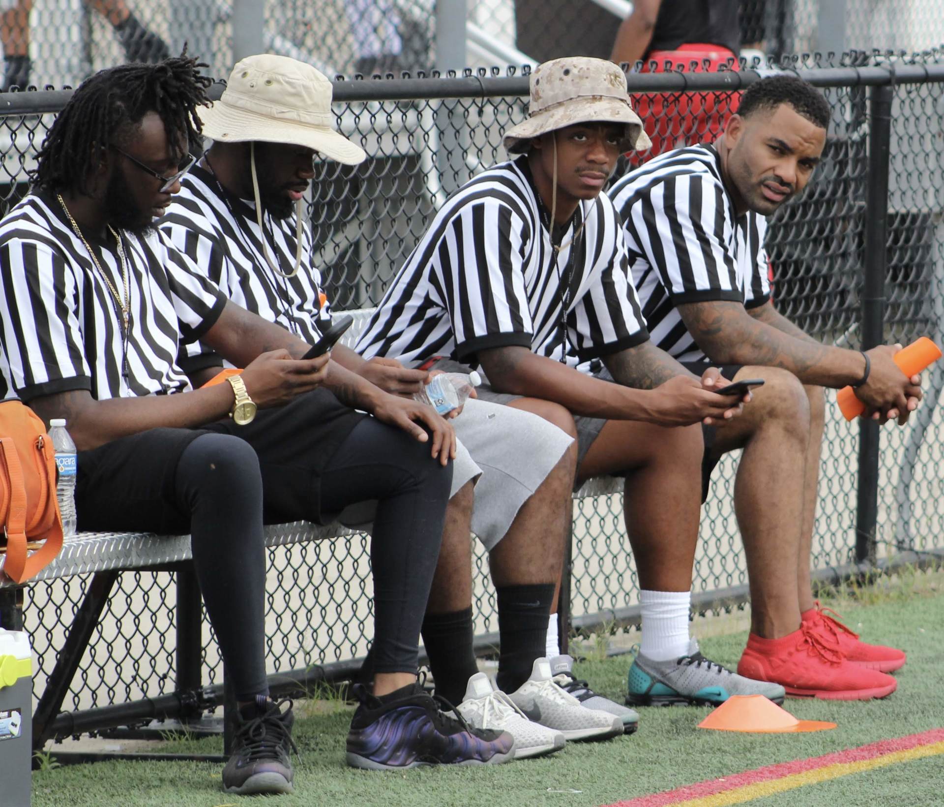 A group of referees are sitting on a bench looking at their phones