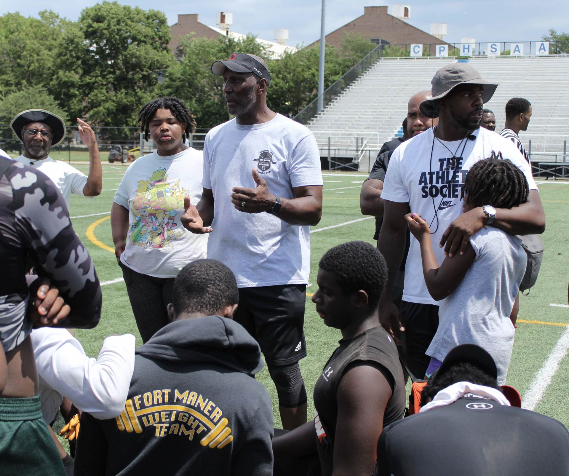 A group of people standing on a field with one man wearing a shirt that says the athletic society