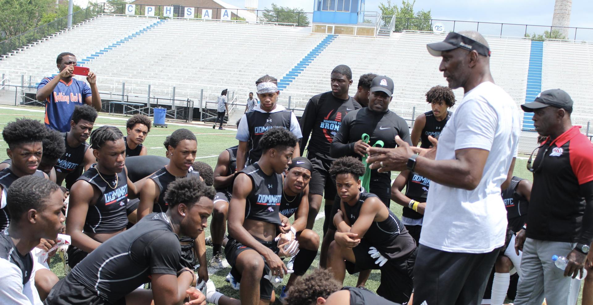 A man is talking to a group of young men on a football field.