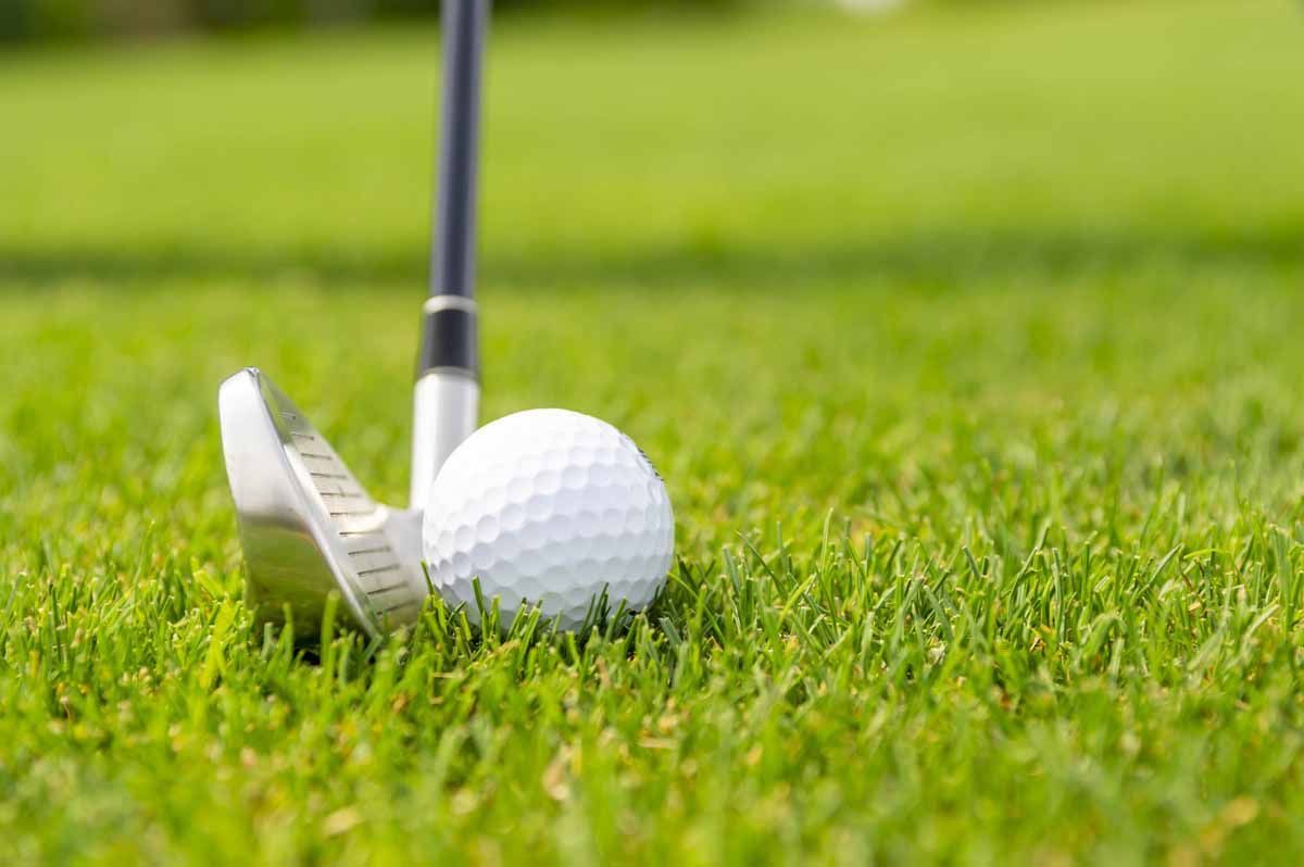 Golf ball on green grass with golf club.