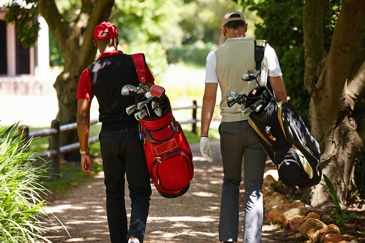 Two golfers walking on a path, carrying golf bags.