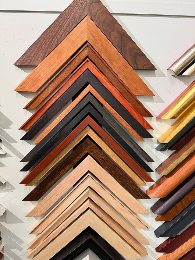 A wall display of V-shaped wooden frame corner samples in various wood tones, finishes, and profiles.