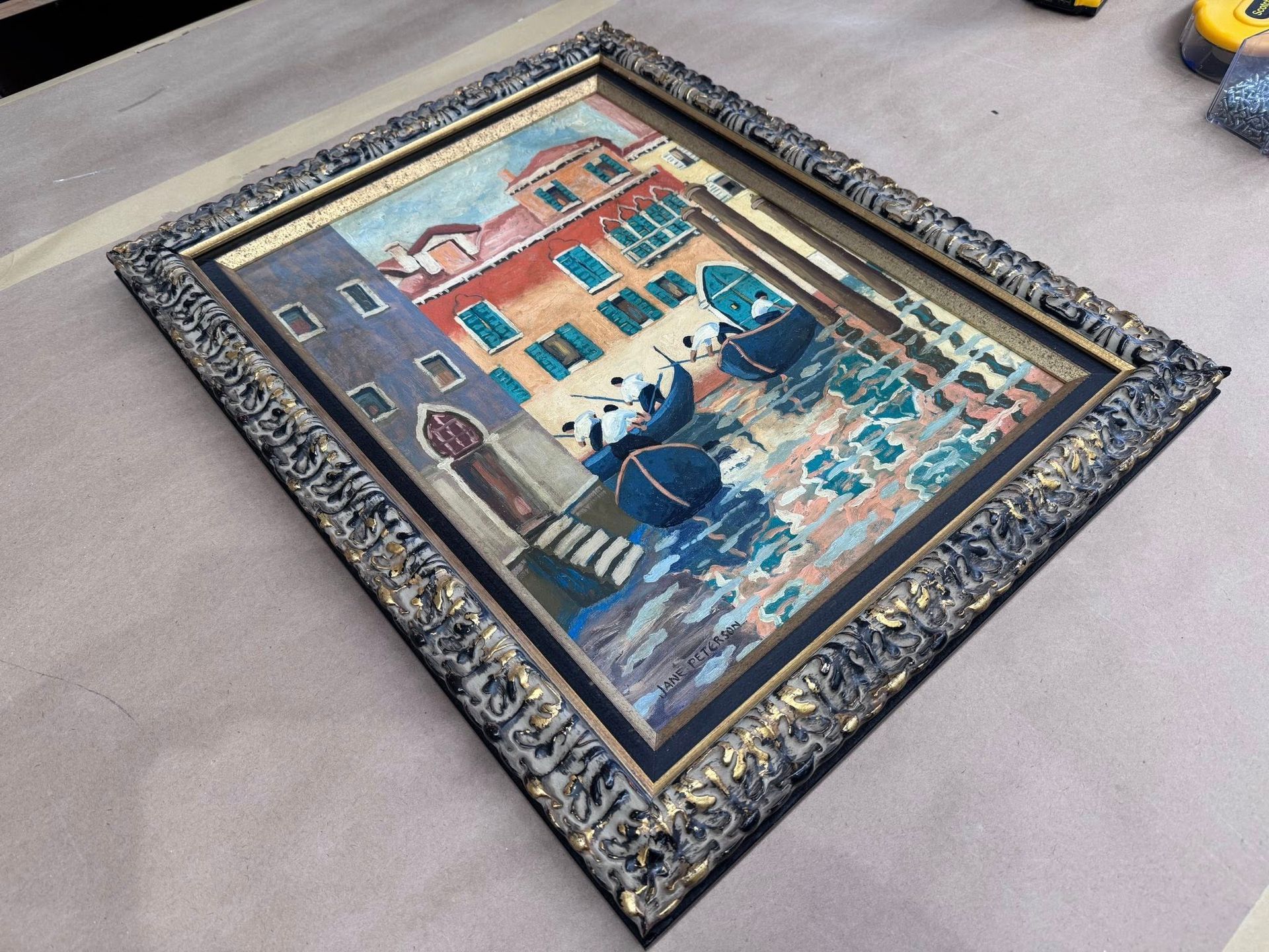 A framed painting of a Venetian canal scene featuring colorful buildings, gondolas, and blue water, angled on a surface.