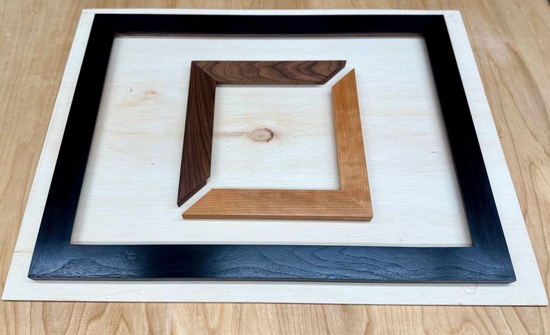 A Stanley tape measure, a small hammer, and two wooden frame pieces joined at a corner with adhesive on a wooden surface.