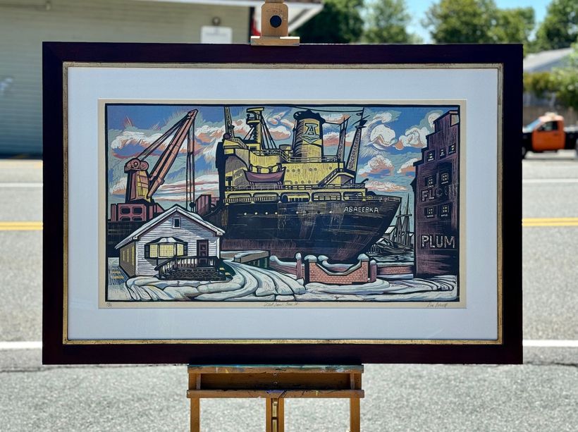 Framed woodblock print of a large industrial ship docked beside a small house and a factory building with a crane.
