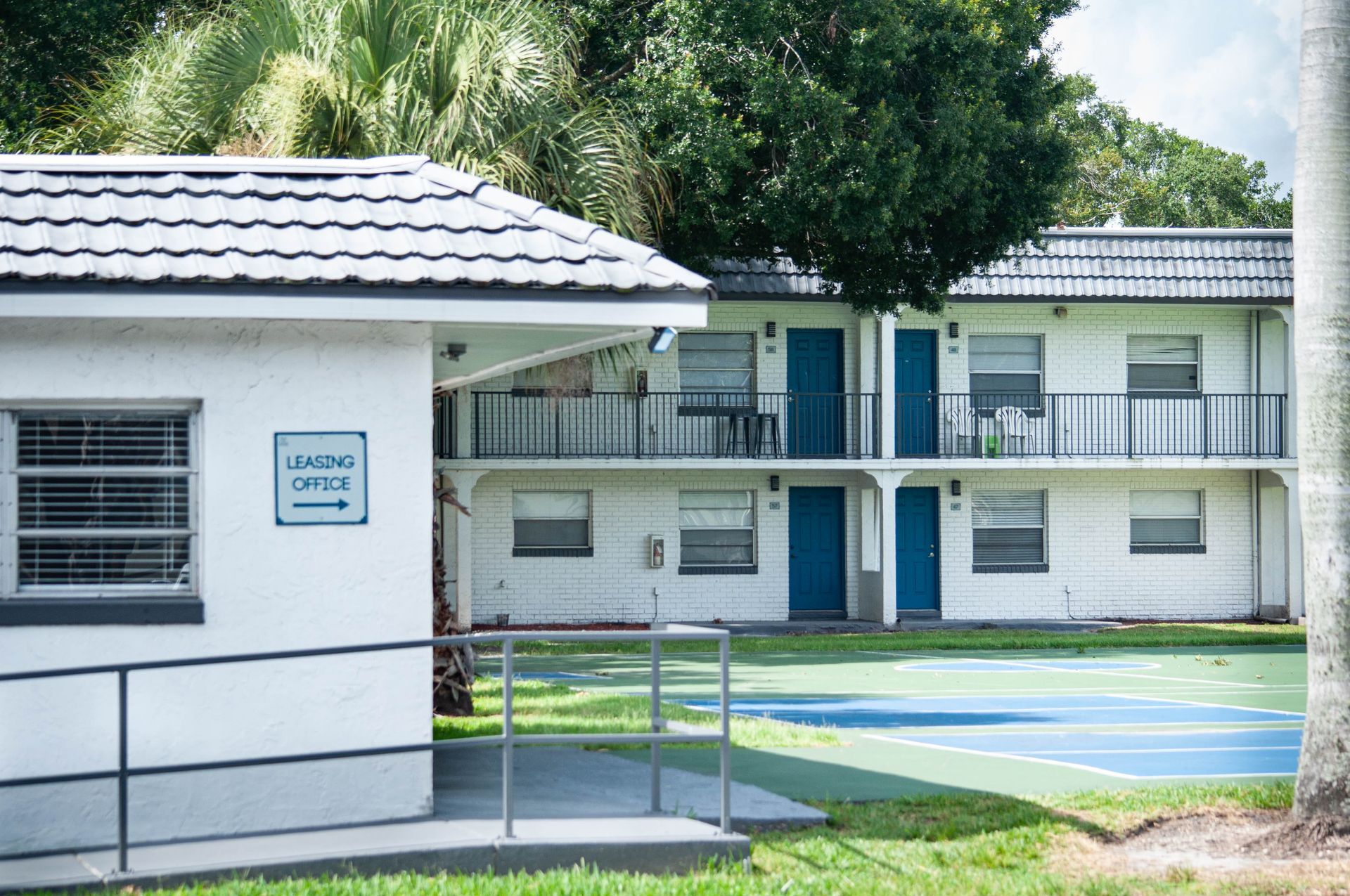 A white building with blue doors and a tennis court in front of it.