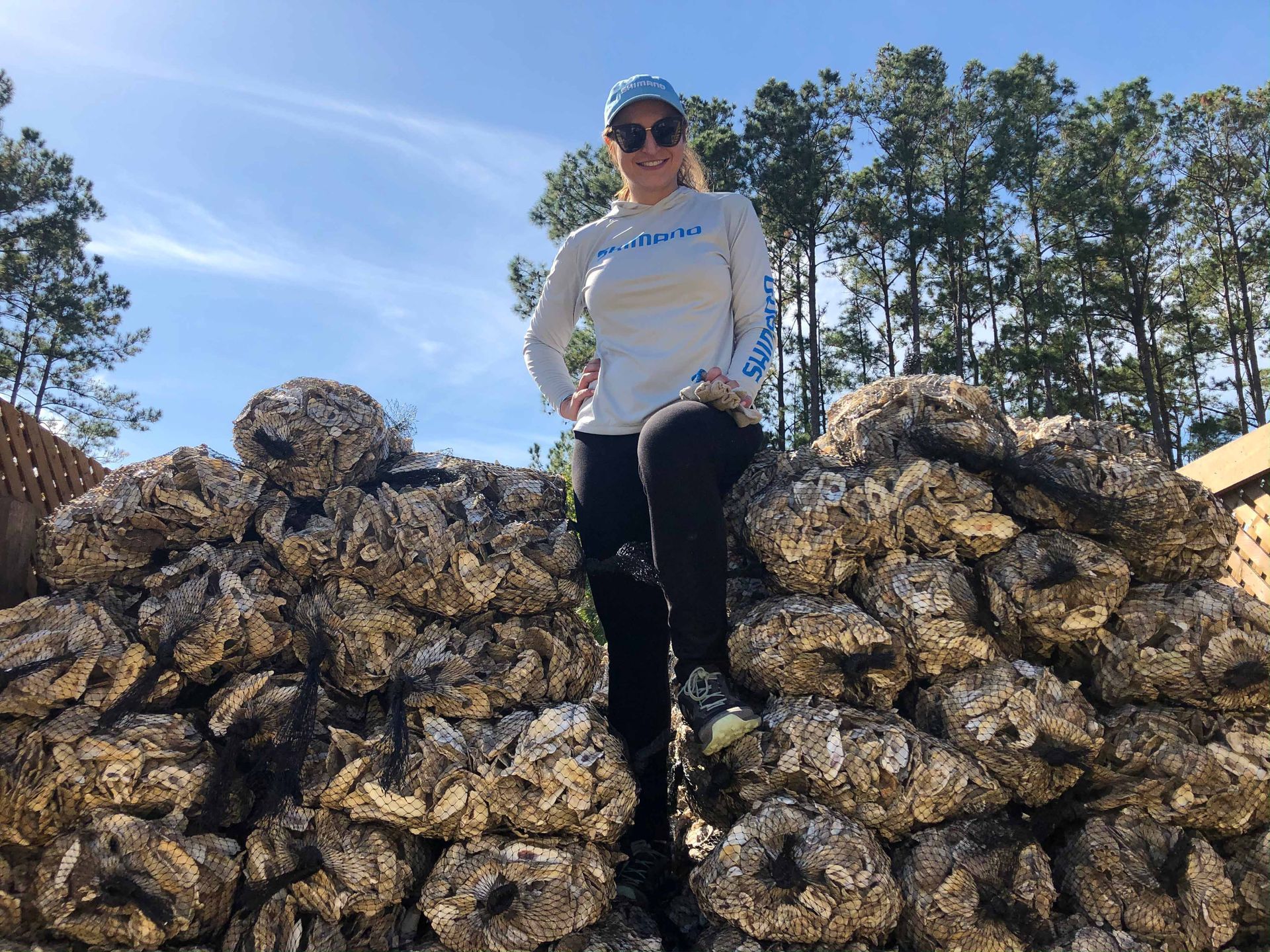 a woman wearing a shimano shirt stands on top of a pile of oysters