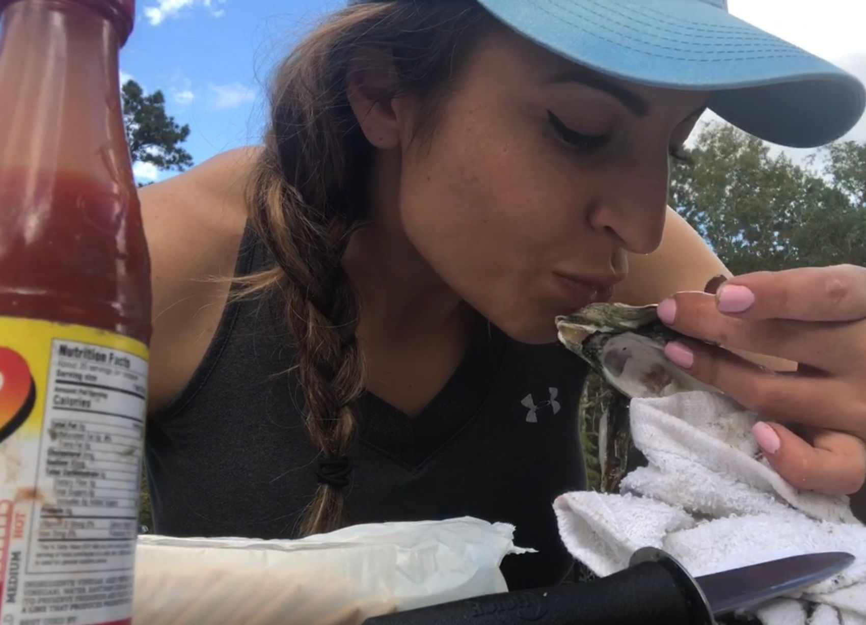 a woman is eating an oyster next to a bottle of medium hot sauce
