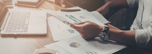 Person reviewing documents at a desk with a laptop, analyzing documents and business.