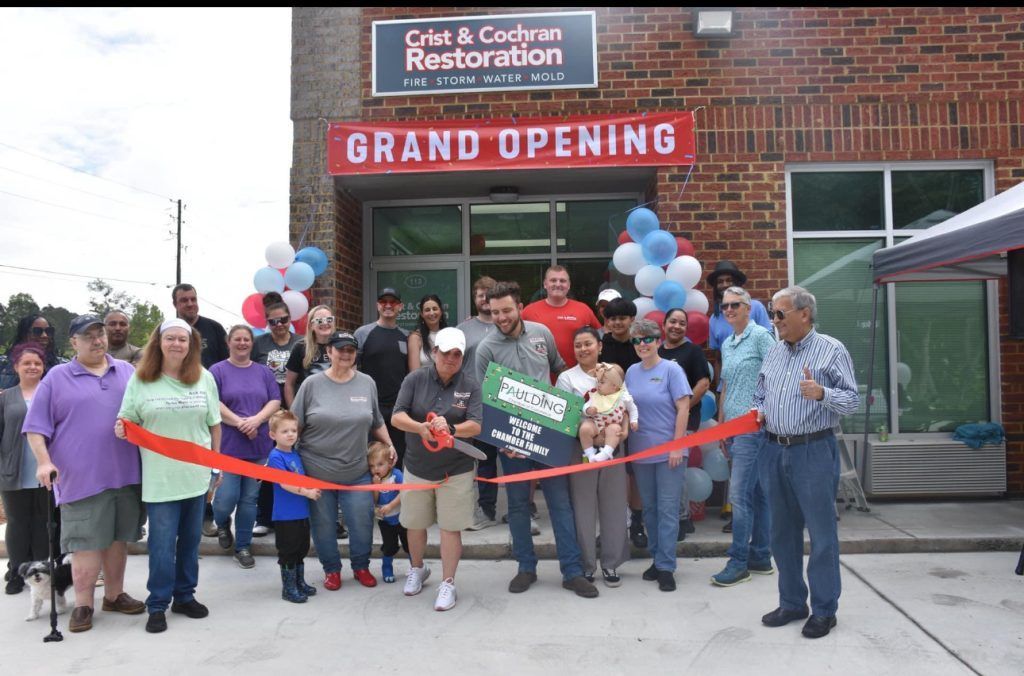 A group of people are cutting a red ribbon in front of a building that says grand opening