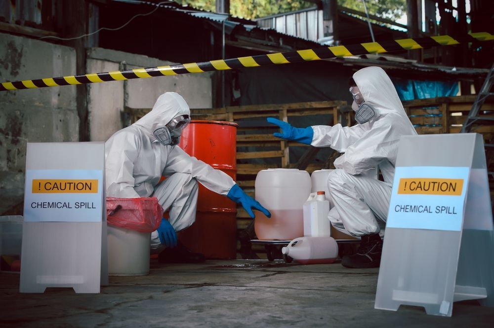 Two people in protective suits are sitting next to a sign that says caution.