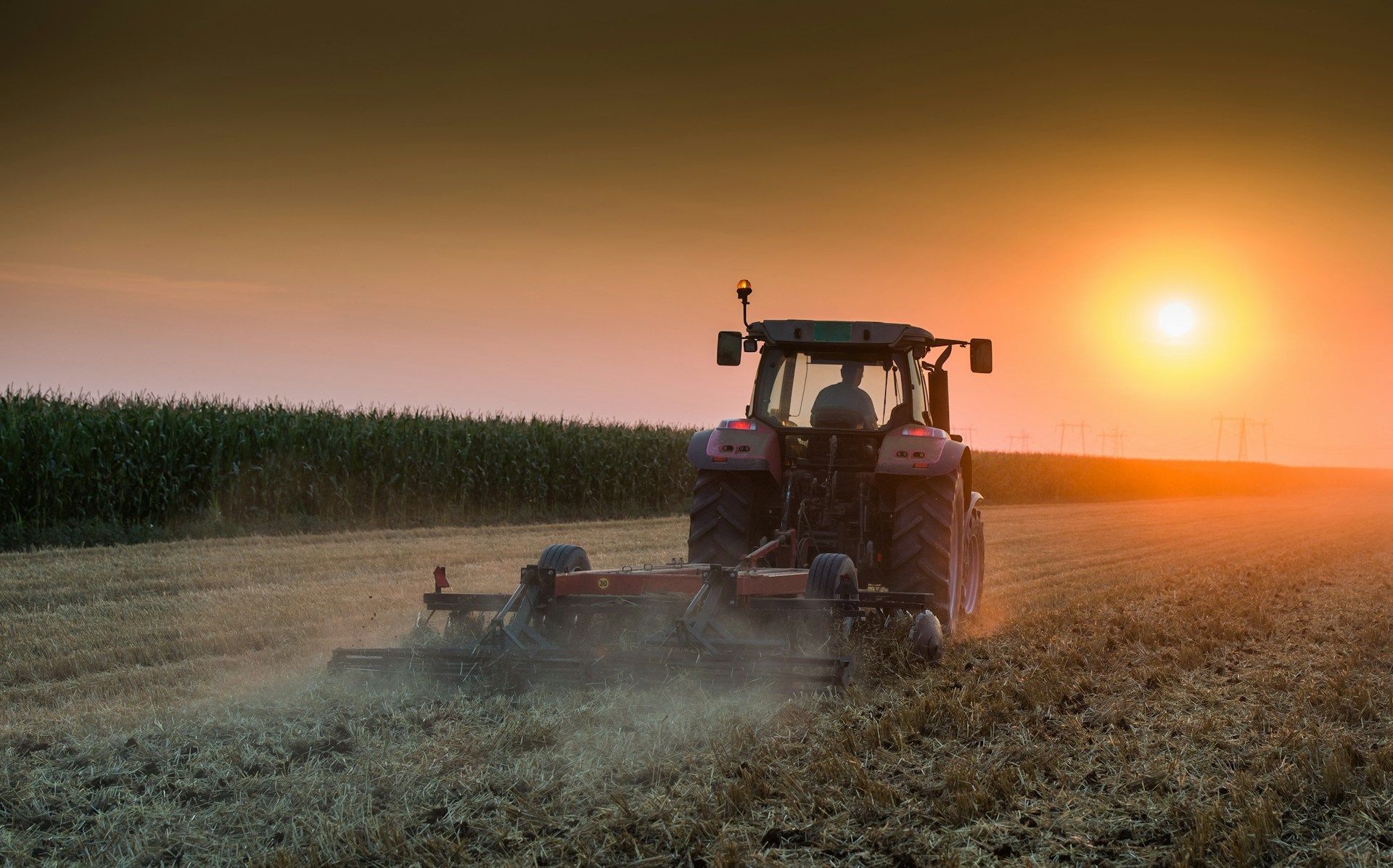 Tractor plowing a field at sunset, kicking up dust; golden light.