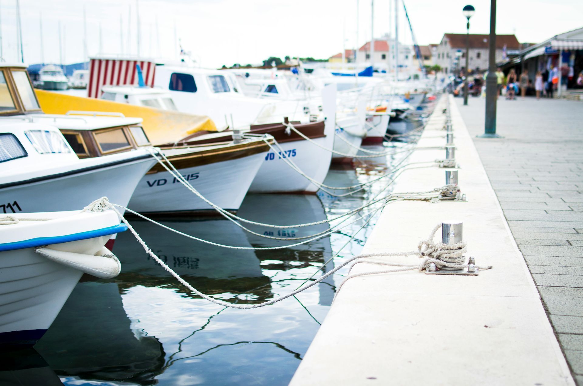 Boats docked at a pier, with white hulls, blue water, and a blurred background of buildings.