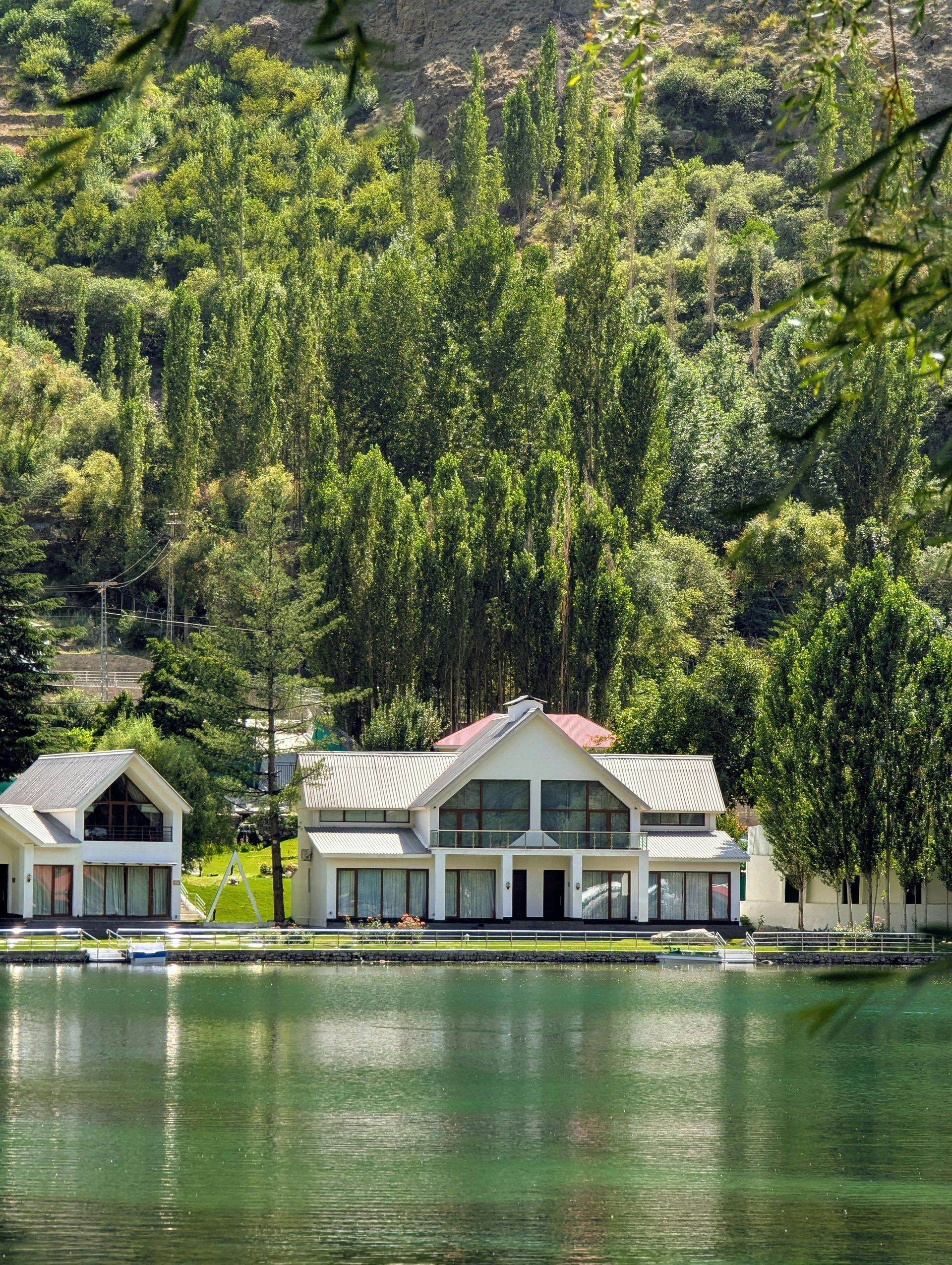 Two white houses with lake view, backed by green trees and a mountain.