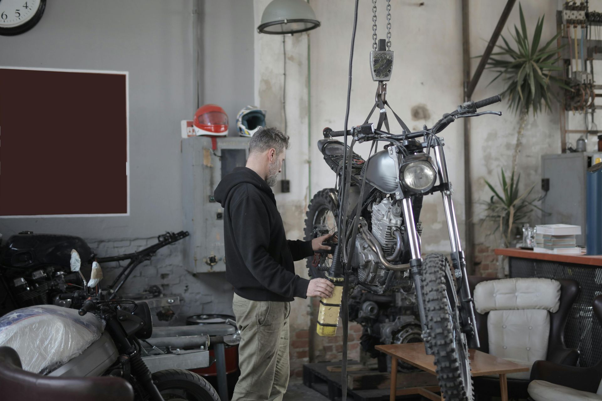 Man working on motorcycle in a garage, bike suspended from a hoist.