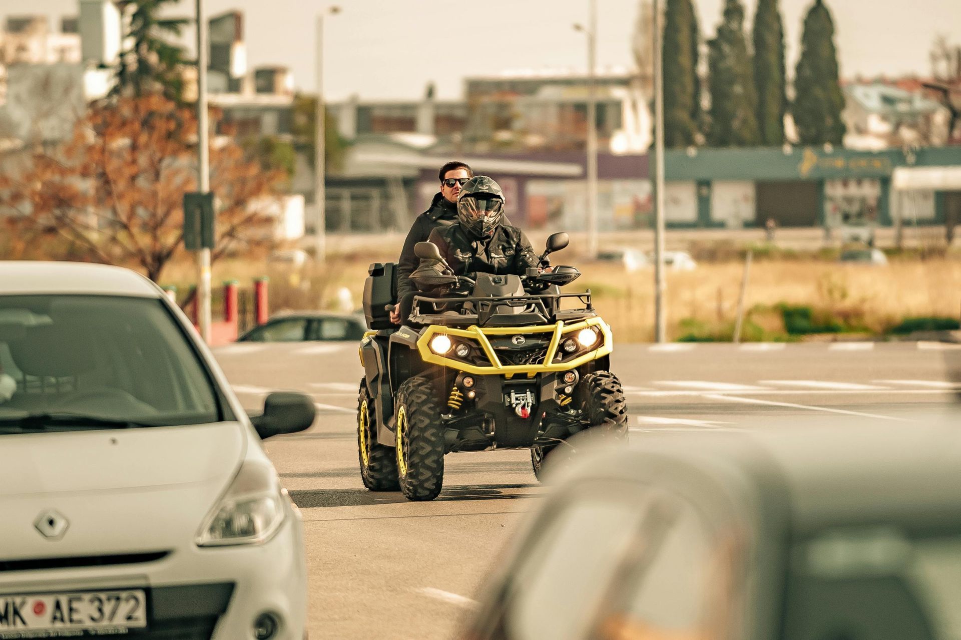 Two people on a yellow and black ATV driving on a road with cars.