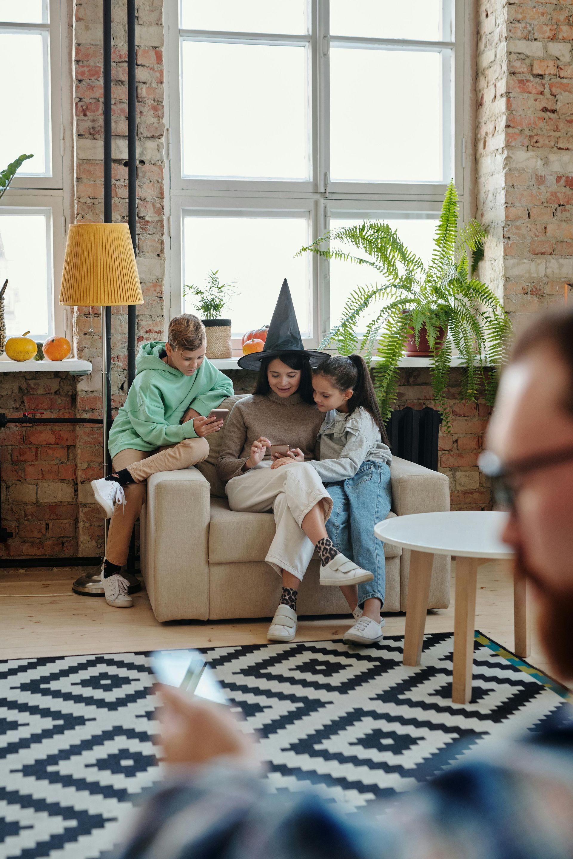 People sitting on a couch looking at a phone, with a boy, and girl beside them.
