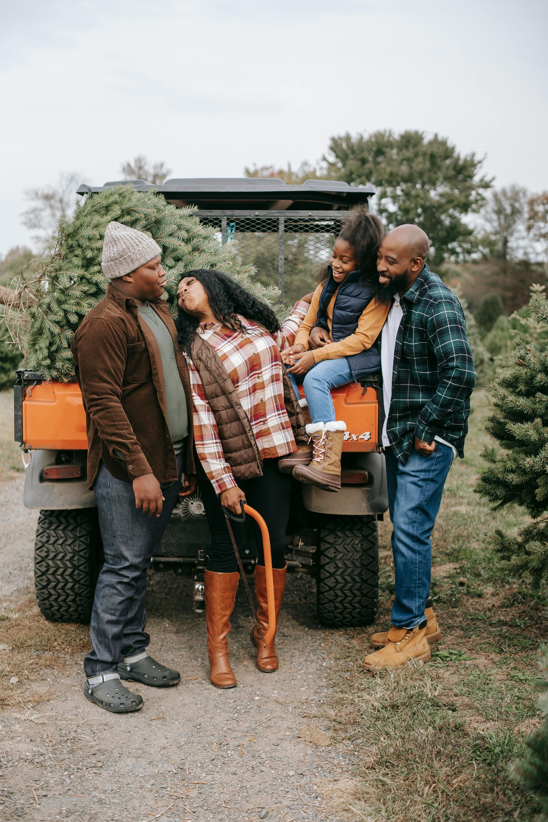 Family poses next to an orange ATV, a Christmas tree in the back. Smiles, outdoor setting.