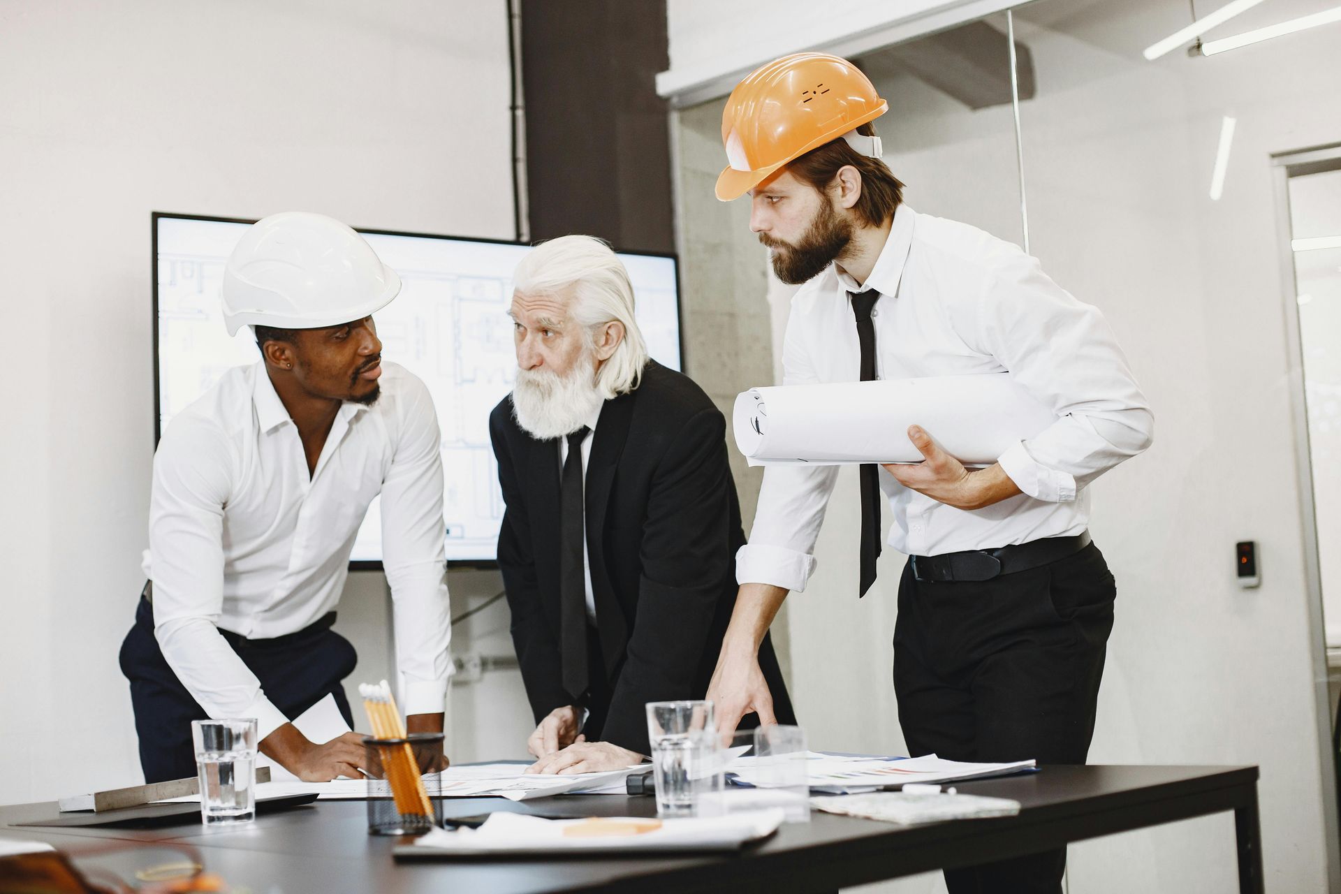 Three people in a meeting, wearing hard hats and looking at plans on a table.
