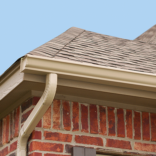 A brick house with a tan gutter and a brown roof