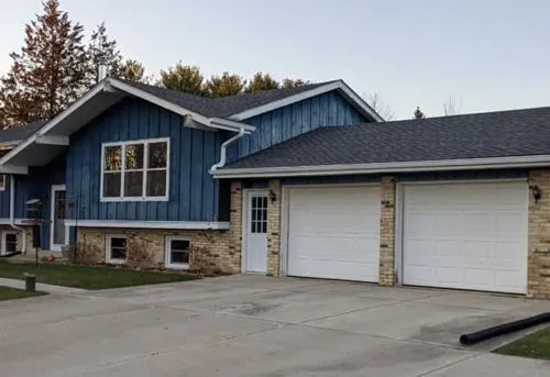 A blue house with two white garage doors and a gray roof.