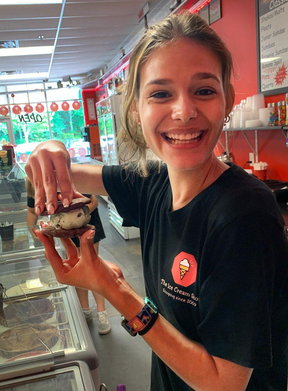 A woman in a black shirt is holding an ice cream cone in her hand.