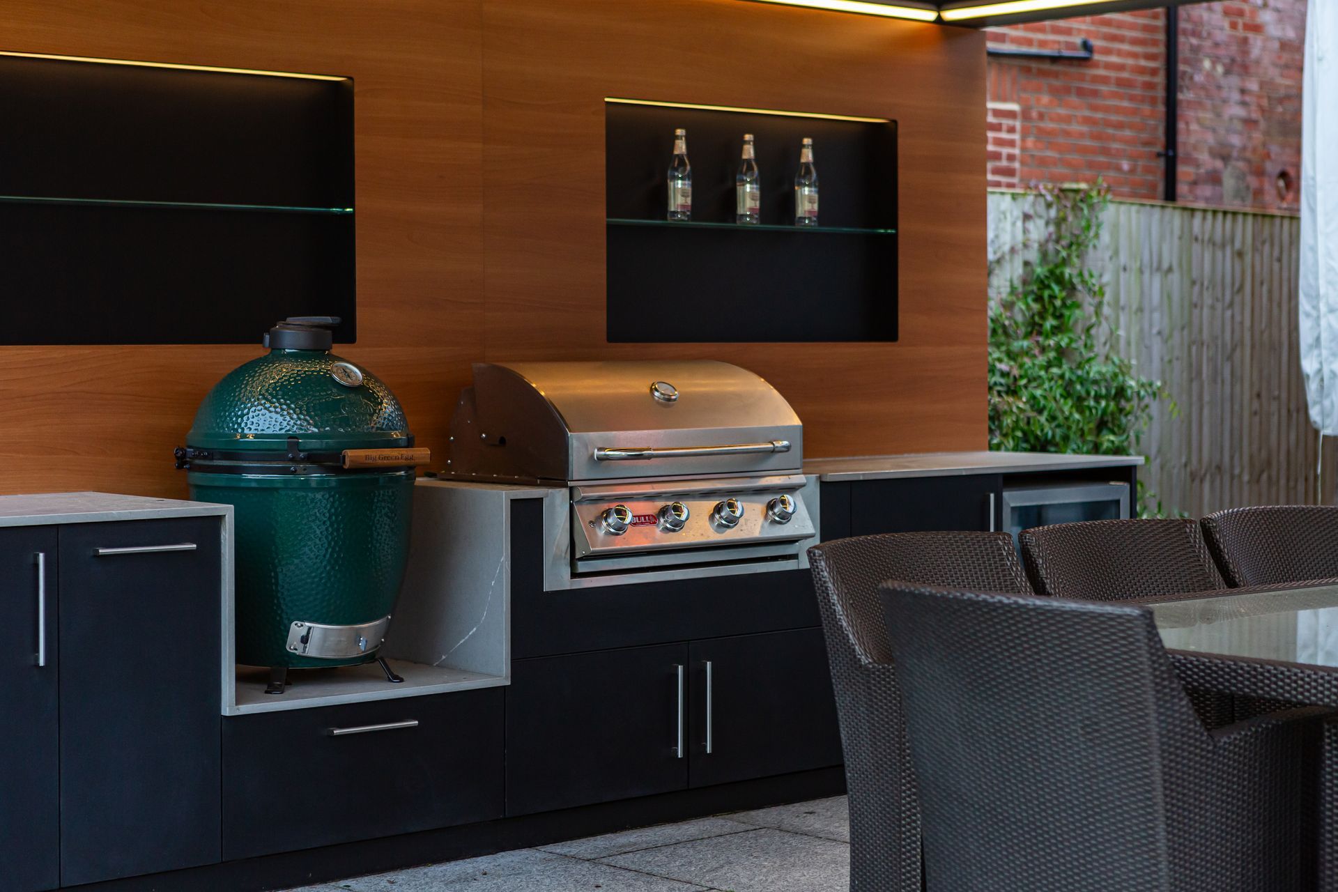 Outdoor kitchen with a green smoker, grill, and storage cabinets.