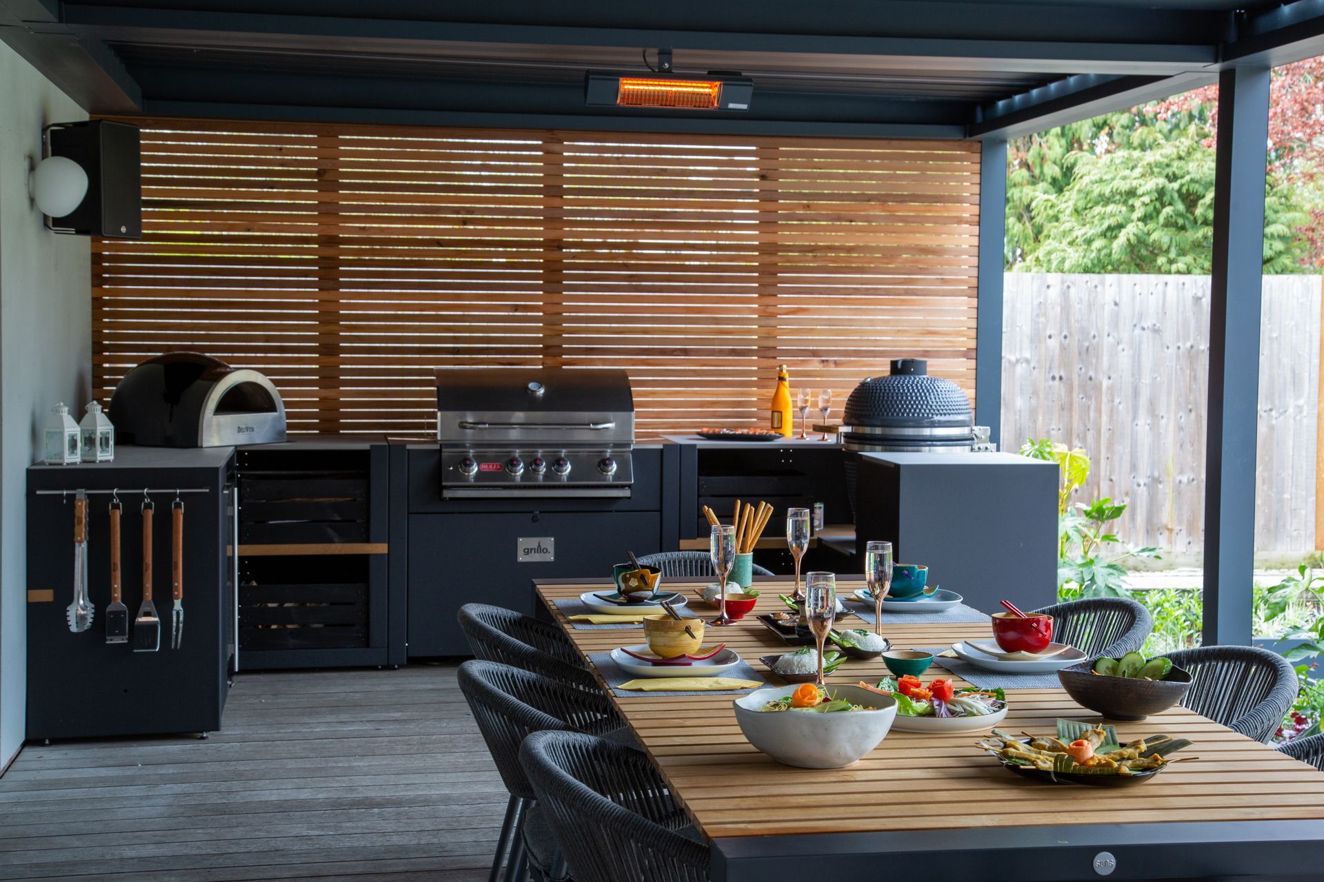 Outdoor kitchen with grill, pizza oven, and dining table set for a meal.