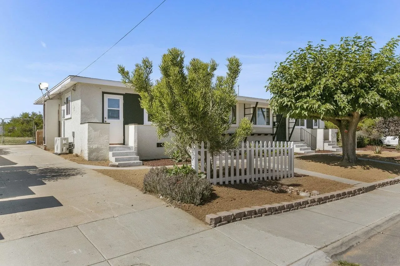 A white house with a white picket fence and trees in front of it.