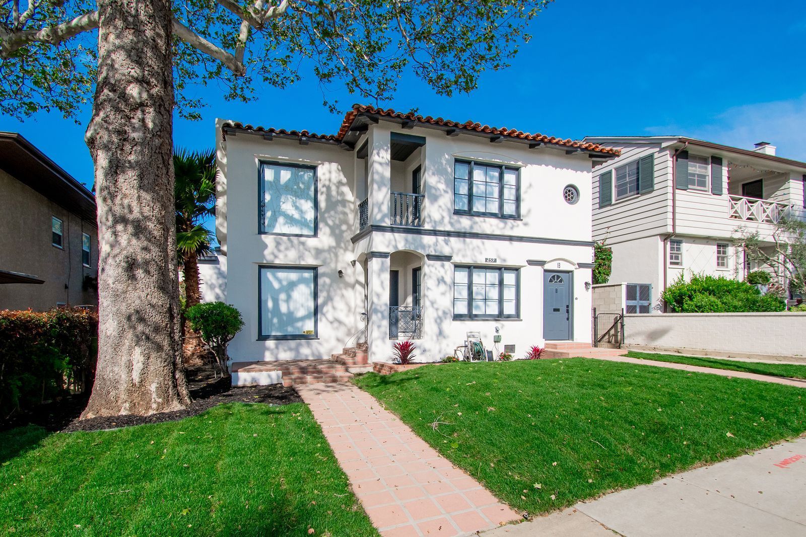 A white house with a lush green lawn and a tree in front of it.