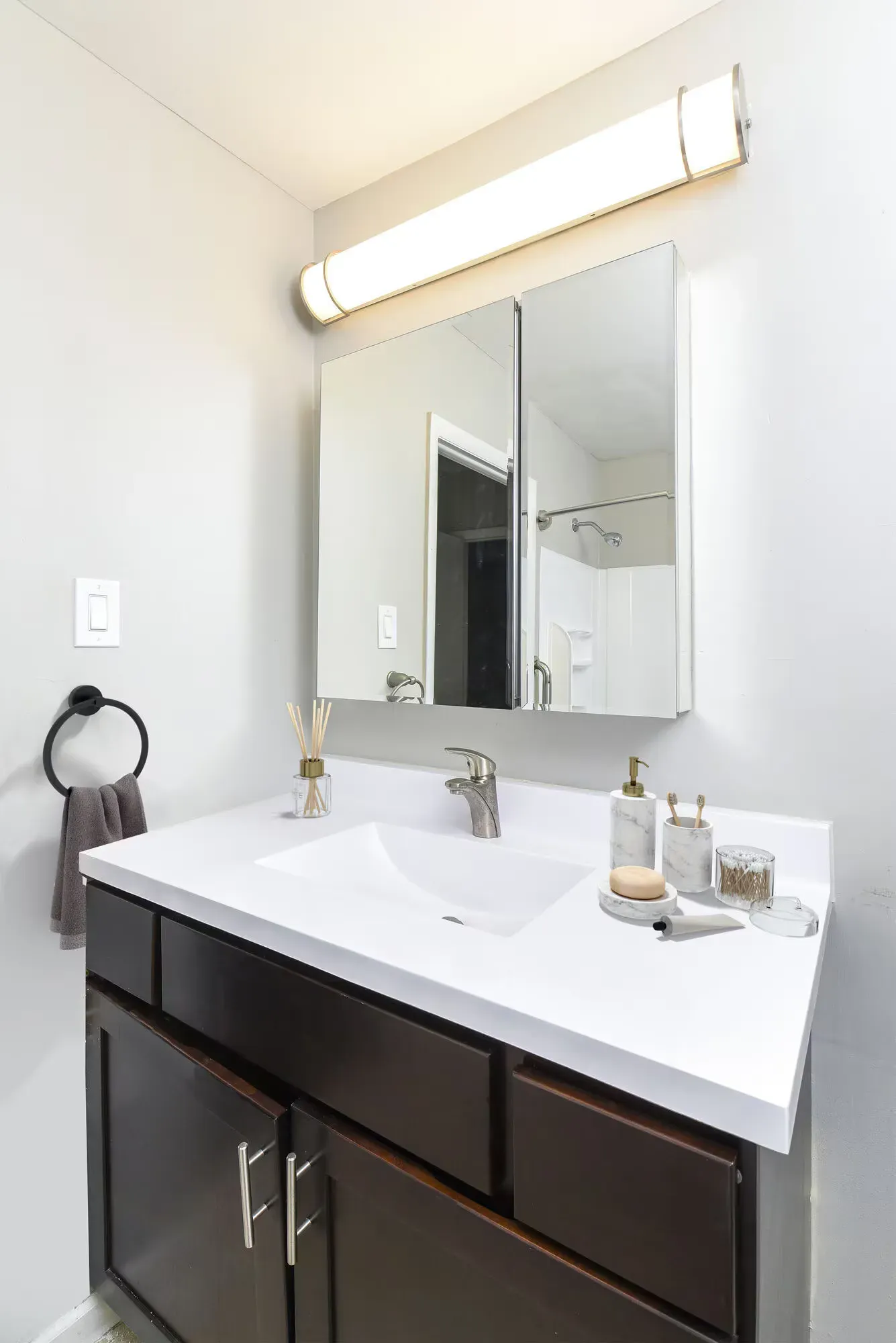 Bathroom vanity with white countertop, single sink, bronze faucet, and mirrored cabinet.