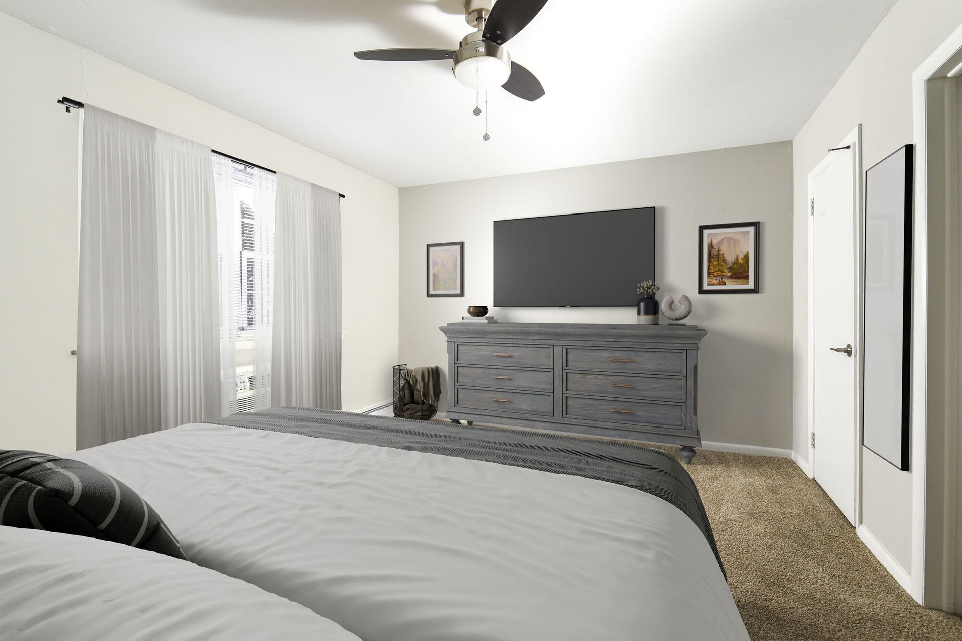 Bedroom with a large bed, gray dresser, wall TV, and sheer curtains.